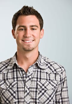 A young man wearing a plaid shirt is smiling at the camera.