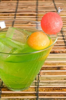 Midori cocktail on ice, garnished with watermelon and cantaloupe.