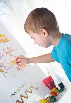 The boy draws with interest paints on a white cloth