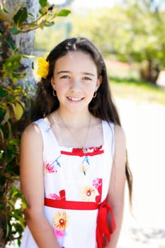 A portrait of a pretty, smiling, dark haired young girl outdoors in a nature setting.