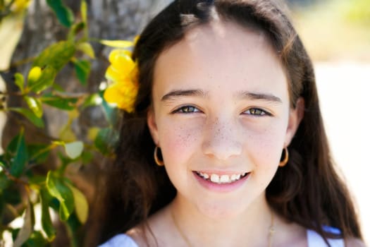 A close-up portrait of a pretty, smiling, dark haired young girl outdoors.