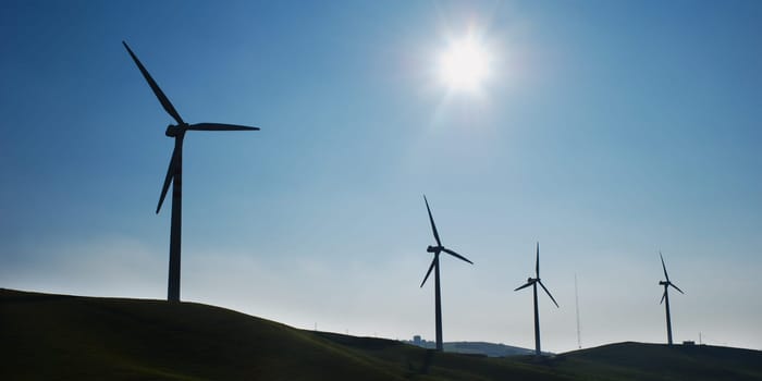 Four wind turbines silhouettes on top of hill