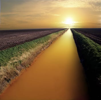 Straight and narrow river flowing towards infinity and the sunset. Looking like liquid gold