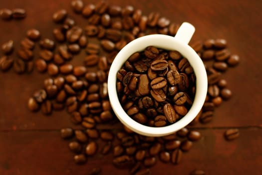 Small white cup filled and surrounded by coffee beans.