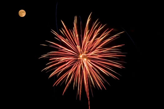 A red and yellow fireworks bursting near the moon.