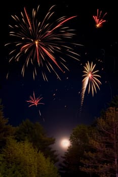 Multiple fireworks exploding above the moon and trees