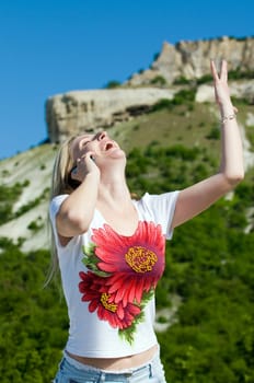 an enraptured girl is speaking on the mobile in the mountains
