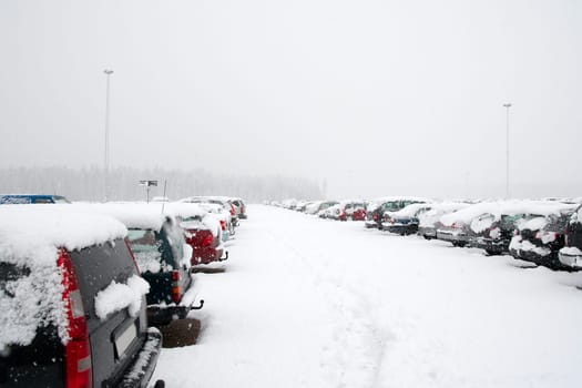 Cars in a parking lot getting covered by snow