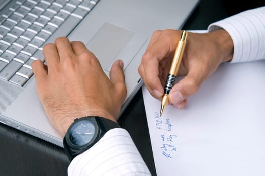 A close-up of a businessman's hands working on a computer and writing down ideas.