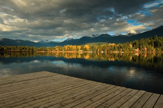 A cloudy autumn scene, is reflecting on the lake surface at the end of the quay in Whisler, British Columbia