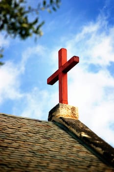 Cross on church roof top with a blue and white sky in background.