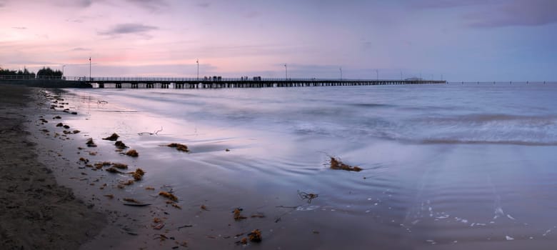 The sunset light is fading over the long pier