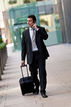 Successful bussinessman travelling with his suitcase and talking on his cell phone. Shot on location in a city or airport setting.
