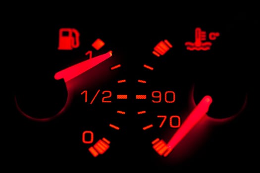 Car dashboard gauges illuminated over a black background. Shallow depth of field