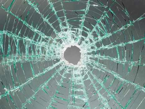 There is a broken car glass of windscreen with hole in picture center