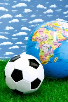 Soccerball on grass with globe over sky background