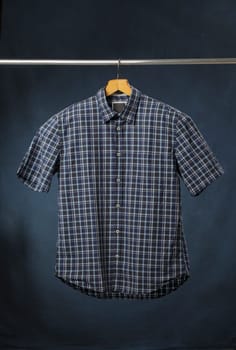 A new men's blue plaid cotton shirt hanging on a hanger.
