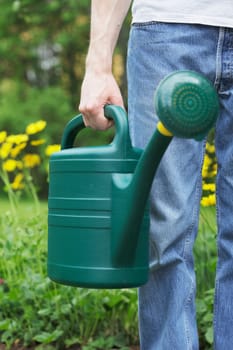 A Man holding a green plastic watering can in his hand. Short depth of field, sharpness is in the hand.