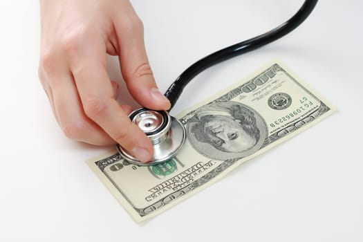 Doctor holding stethoscope in her fingers against one hundred u.s. banknote at the white table