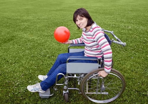 Woman in wheelchair with a red ball in hands
