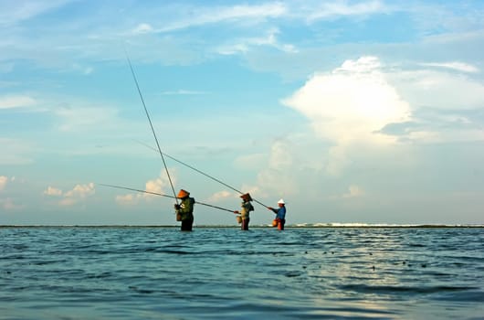 Three fishermen on Bali standing in water and fishing