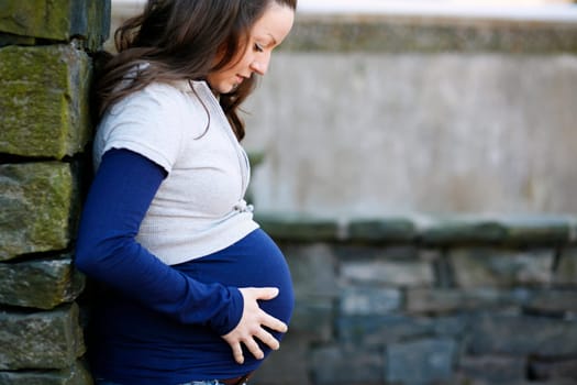 A young pregnant woman holding her time while outdoors.