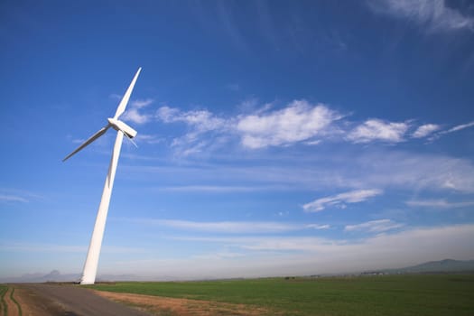 Wind powered electricity generator standing against the blue sky in a green field on the wind farm