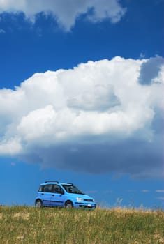 Bright pale blue modern car under white cloud and blue sky
