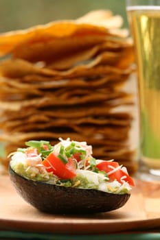 Guacamole in avocado shell with tosatadas and beer in background