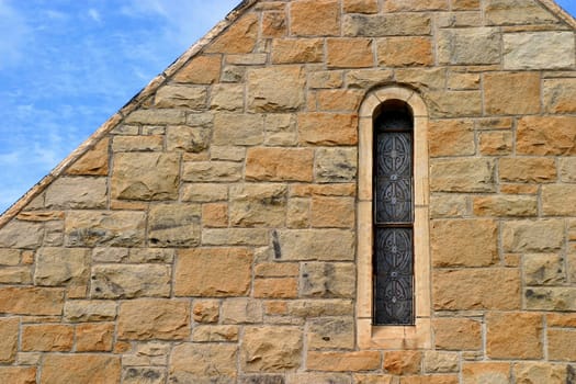Small church window in stone wal with sky.