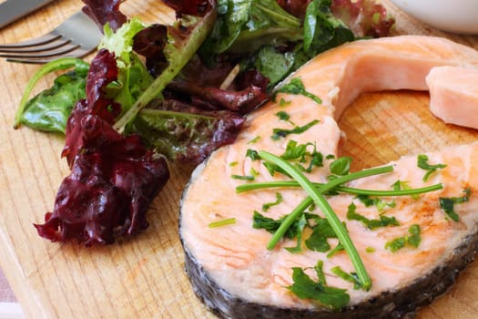 grilled salmon steak on wooden board with salad