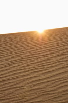sun peaking over ridge of sand dune in Death Valley National Park, CA