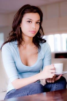 A young woman at home on sofa holding cup and saucer