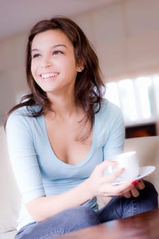 A young woman at home on sofa holding cup and saucer
