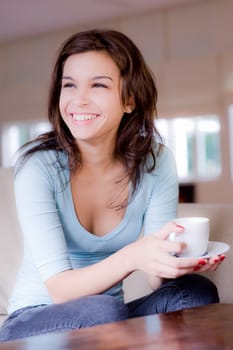 A young woman at home on sofa holding cup and saucer