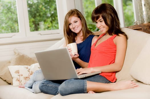 Two young woman at home on the sofa with laptop