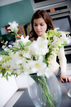 A pretty young woman arranging flowers in the kitchen