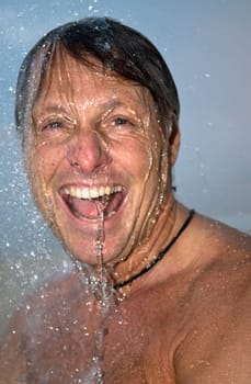 handsome forties man is laughing as he has fun under a powerful shower.