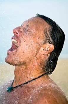 A handsome forties man is taking a wash under a powerful shower at the beach.