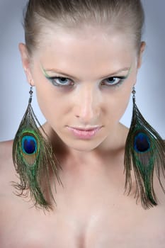 Close-up young blonde model with peacock earrings posing with beautiful make-up
