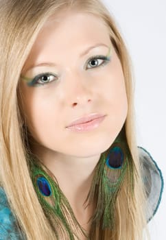 Beautiful young blond model with peacock earrings posing in studio shot