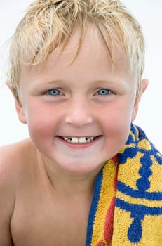 A beautiful blue eyed blonde 8 year old boy is happily smiling for the camera during a day at the beach.