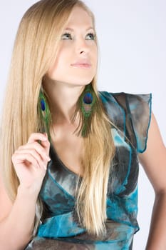 Beautiful young blond model with peacock earrings posing in studio shot