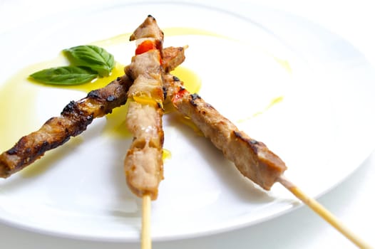 Three little skewers of meat with basil and olive oil
