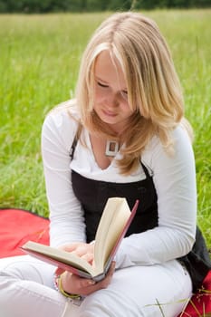 Beautiful young girl reading a book outdoors in the field