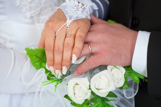 Hands of a newly-married couple with wedding rings against a bunch of flowers