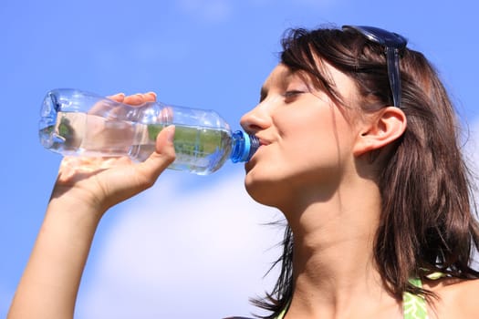 Girl drinking water against blue sky in sunny day