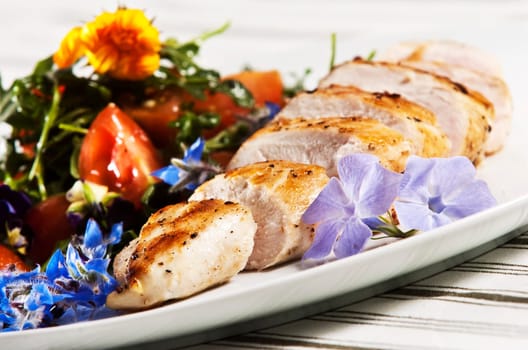 Grilled chicken breast served with salad and garnished with edible flowers