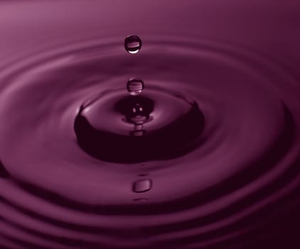 drops of water going into a bigger pool of water that is purple