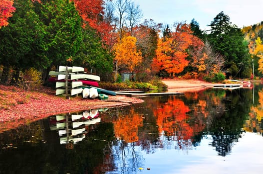 Canoes at forest of colorful autumn trees reflecting in calm lake